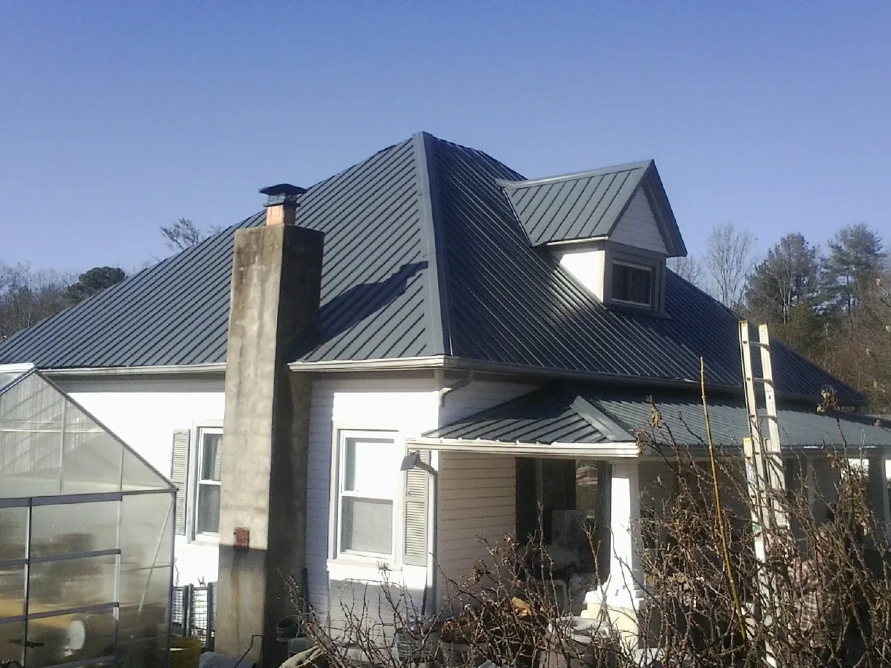 Dark blue standing seam metal roof on a white farmhouse with dormer — Slate & Tile Roof Repair by Roofing Brothers in Goodells