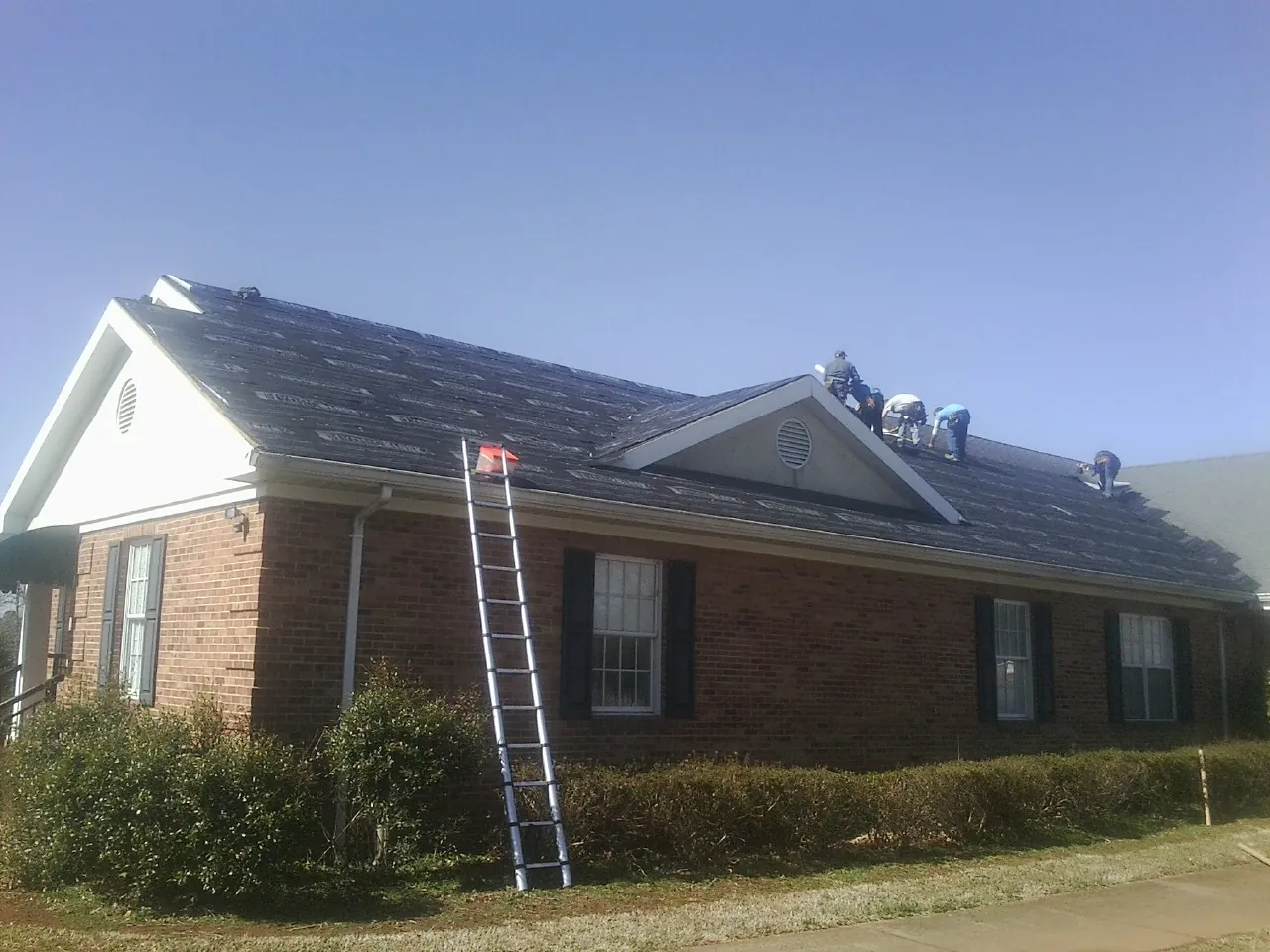 Crew tearing shingles off a brick ranch roof with a ladder set — Emergency Roof Repair work by our crew in Goodells
