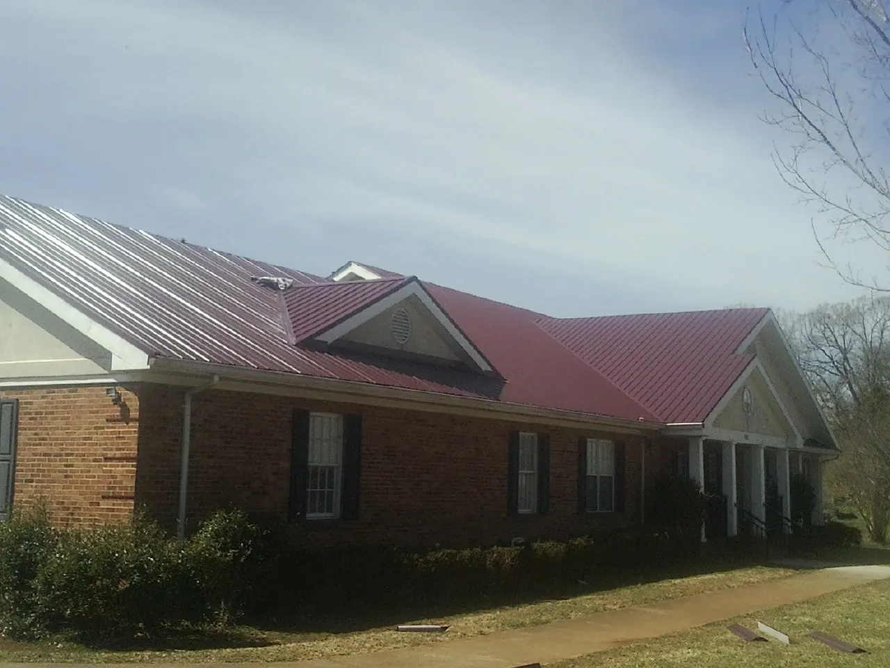 Red metal roof with gabled entries on a long brick building, from a Hail Damage Roof Repair job in Goodells