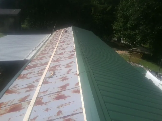 Old rusted panels beside newly installed green metal roofing — Wind Damage Roof Repair by Roofing Brothers in Goodells