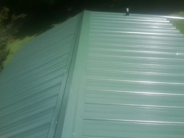 New green metal panels meeting at the ridge of a roof — Flat Roof Repair work by our crew in Goodells