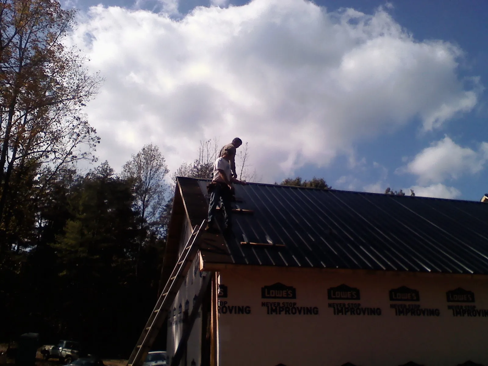 Roofer fastening dark metal panels high against a cloudy sky, from a Roof Inspection job in Goodells