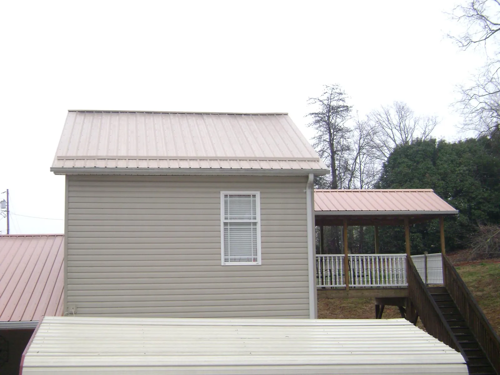Tan metal roofs on a two story addition and attached porch, from a Roof Replacement job in Goodells